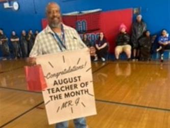 Male teacher holding sign teacher of the month august
